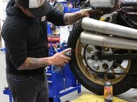 Rotating the tire as he sprays chain cleaner to make sure the entire chain is covered.